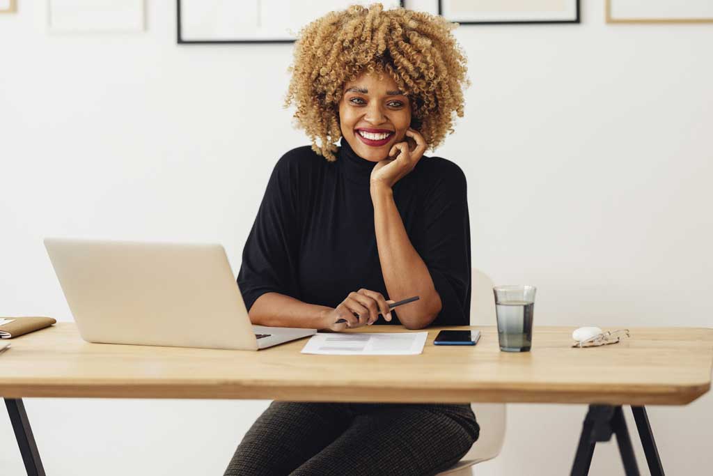 Confident African business woman looking at camera with laptop and pen