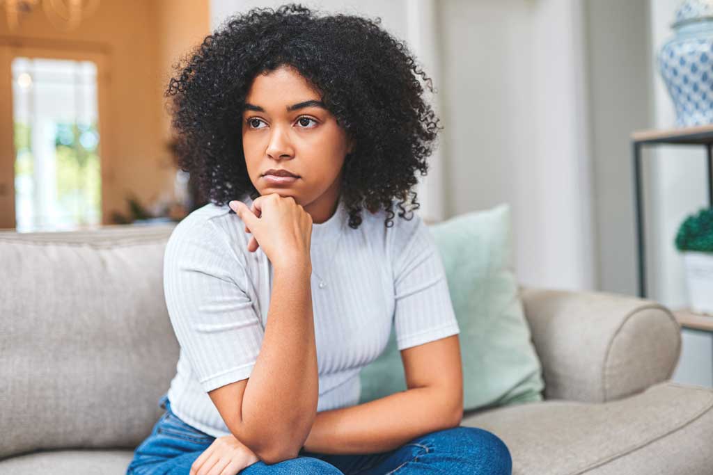 Worried young woman sitting at home on couch