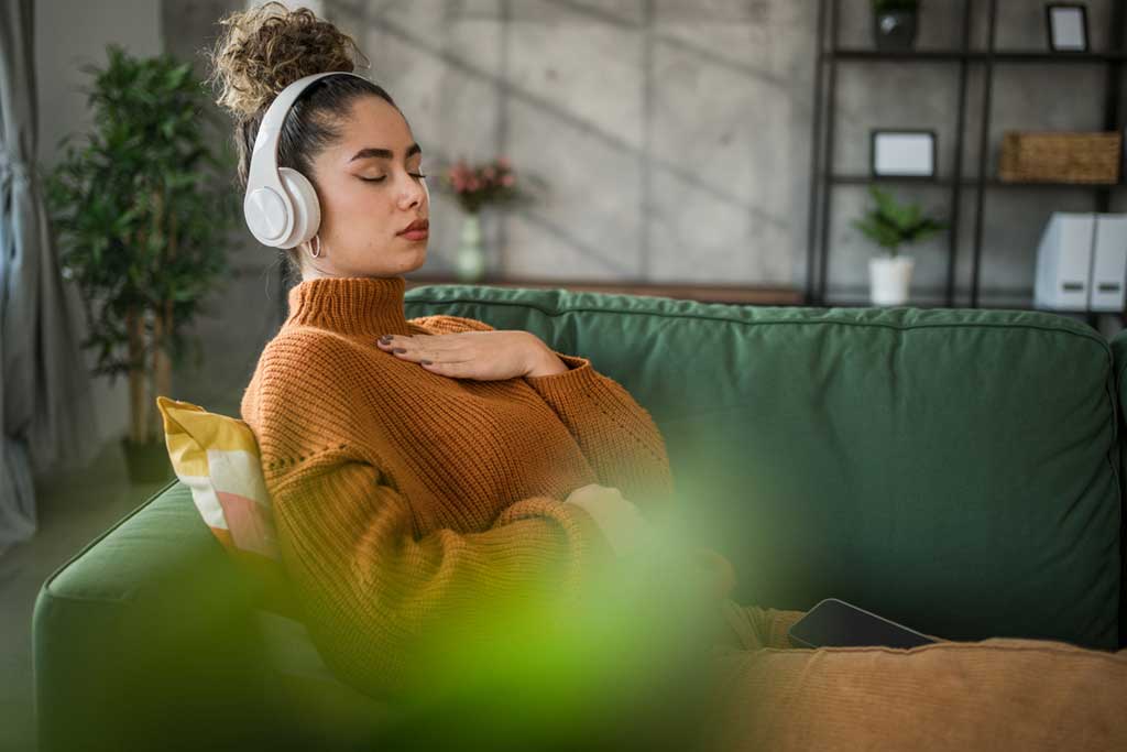 A young beautiful woman practices guided meditation in the living room on her sofa